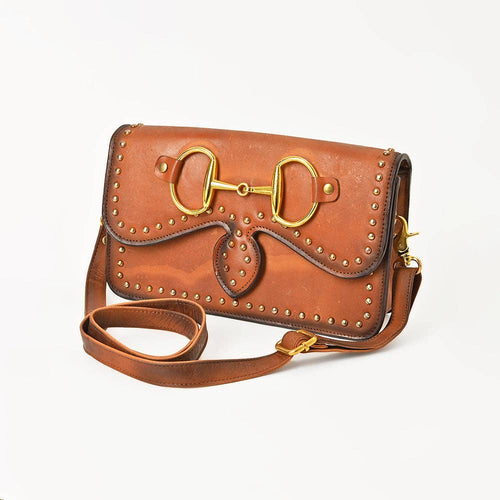 Brown leather crossbody bag with antique-finish equestrian bit hardware and decorative rivets.