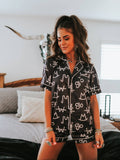 Supplier model wearing the black Western brand-print pajama set with a button-front top and matching ruffle-hem shorts