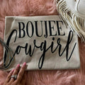 Boujee Cowgirl t-shirt with black lettering, shown in the supplier's styled flat lay