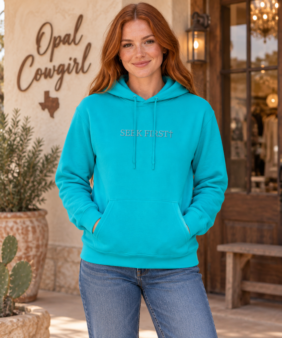 Styled mockup of a red-haired woman wearing the Bright Aqua Seek First embroidered hoodie.
