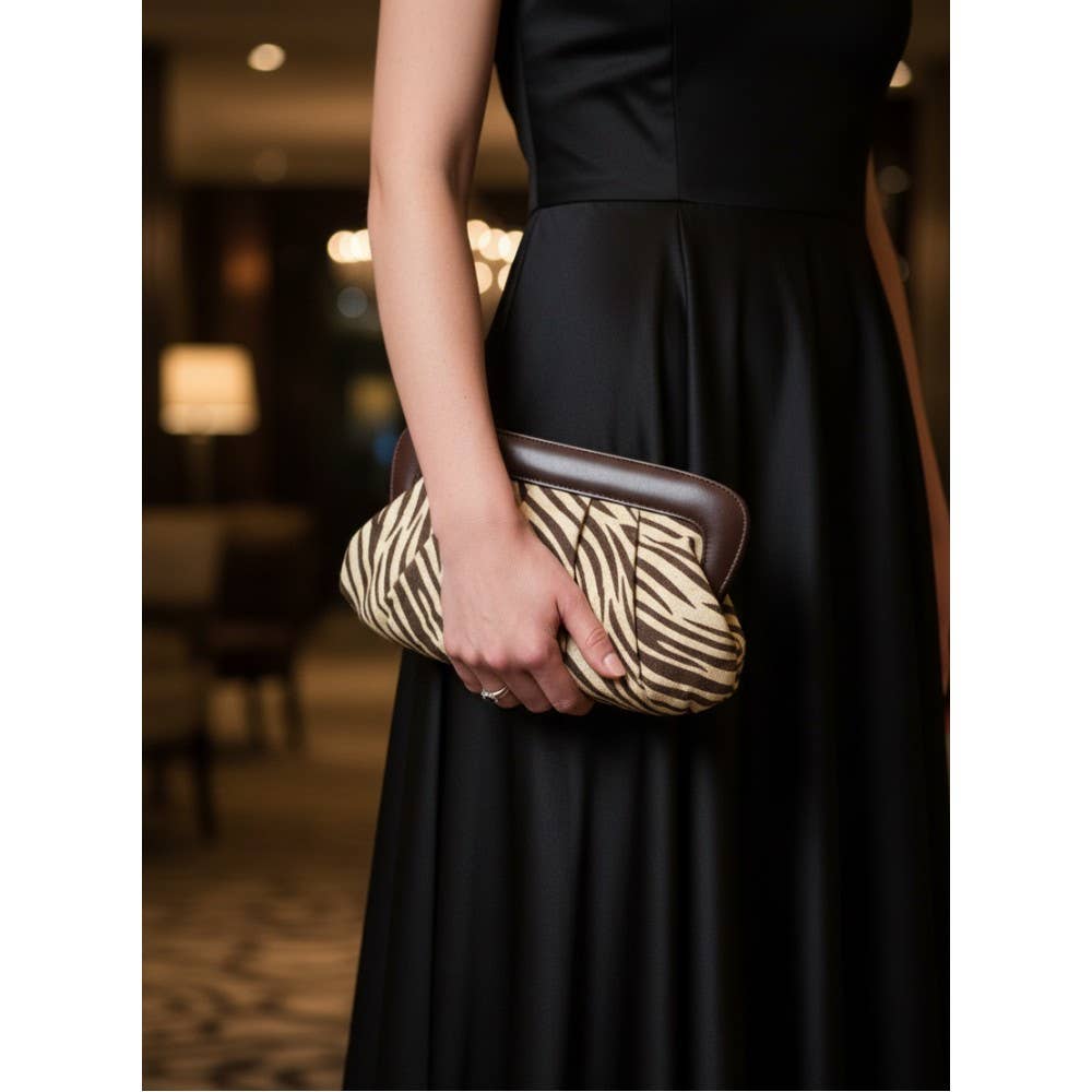 Supplier styling photo showing the brown zebra clutch held in one hand; clutch only.